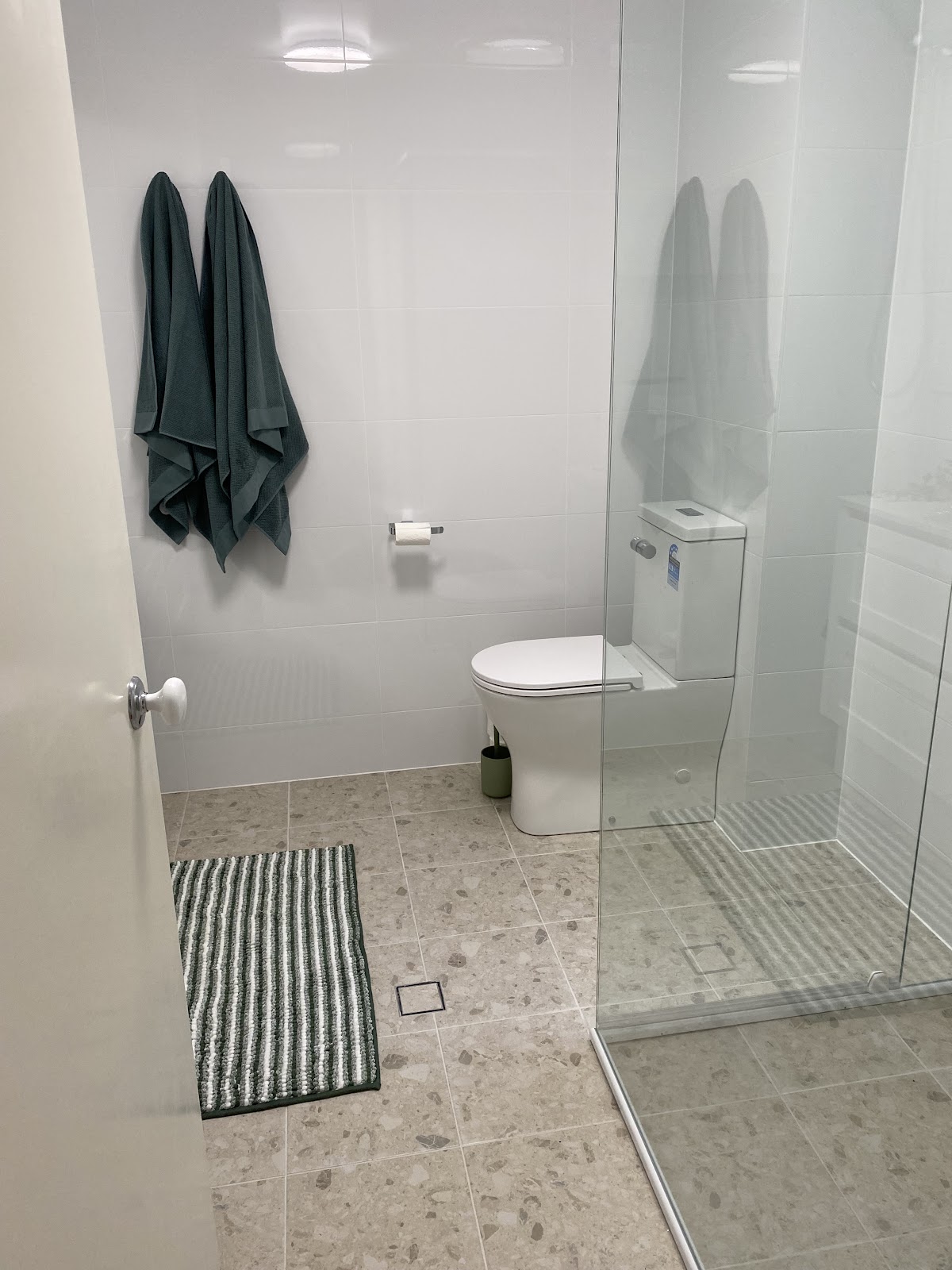 Bathroom with terrazzo floor tiles, frameless shower screen and green towels