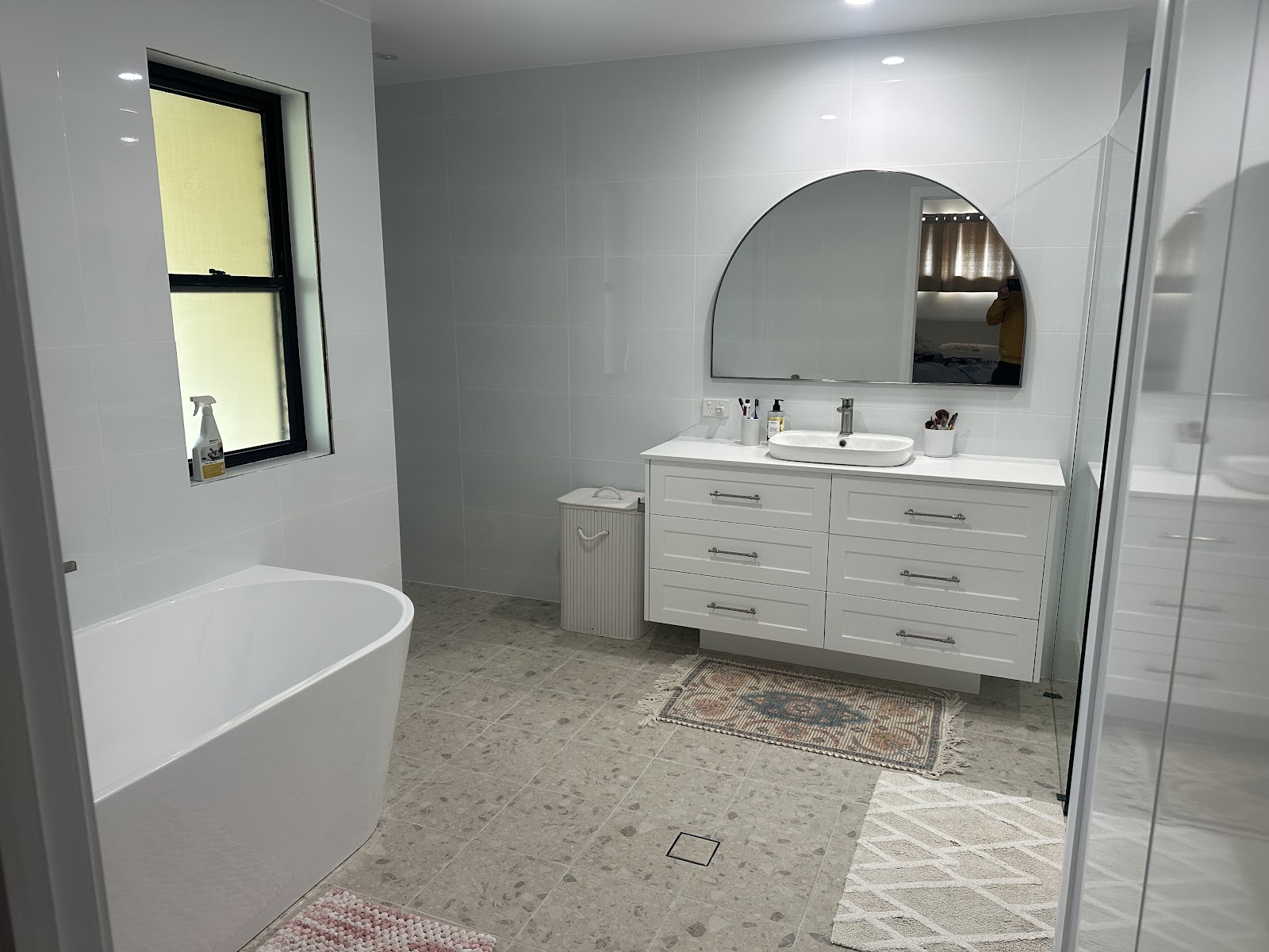 Renovated bathroom with a freestanding bath, white shaker vanity and arched mirror