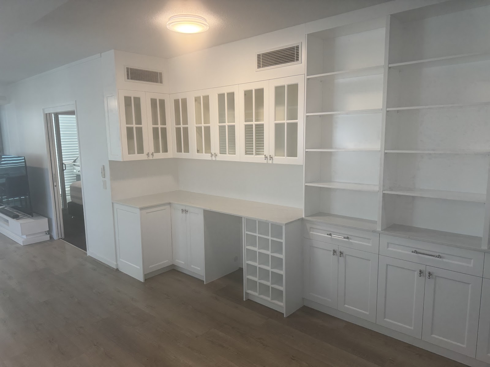 Built-in study wall with glazed upper cabinets, open shelving, a desk and a wine rack
