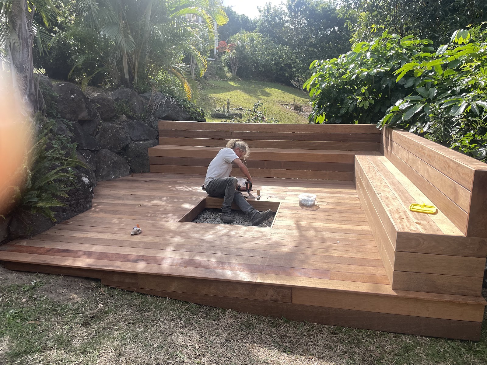 A sunken hardwood deck with built-in bench seating being finished in a sloping garden