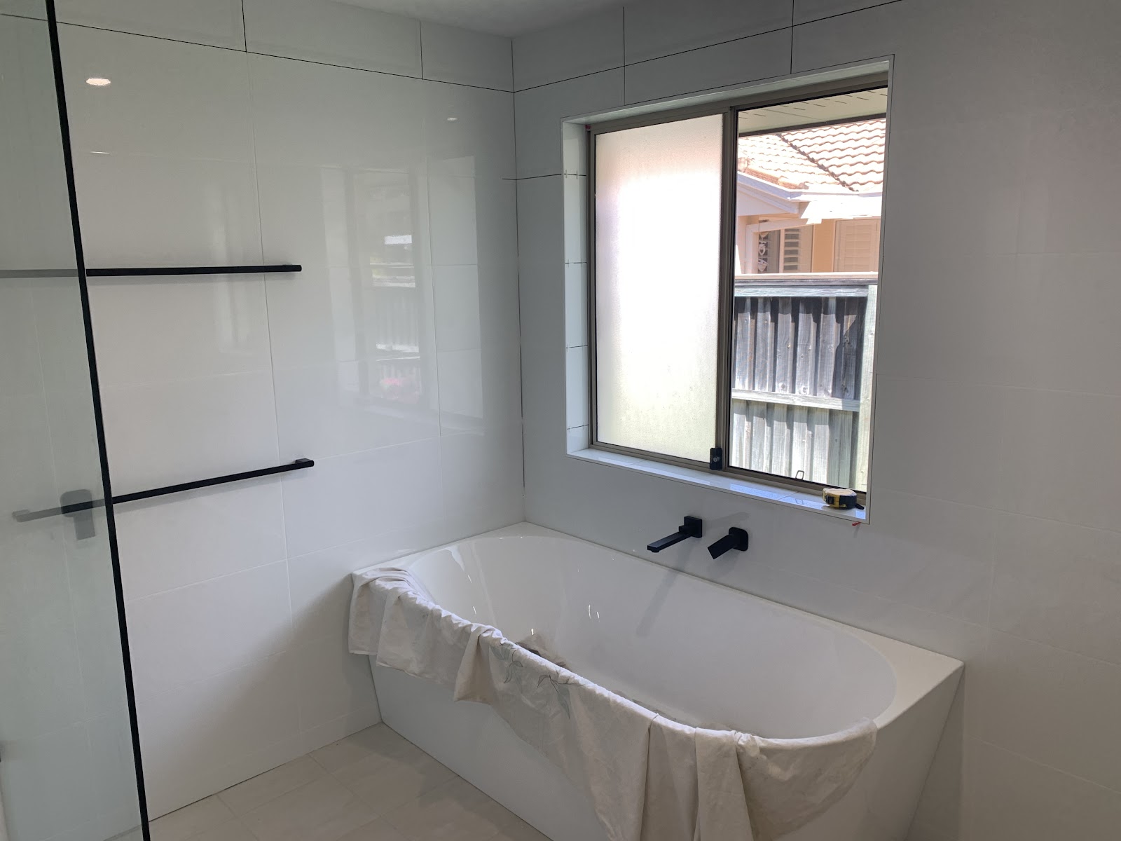 White bathroom nearly finished, bath with black tapware under the window