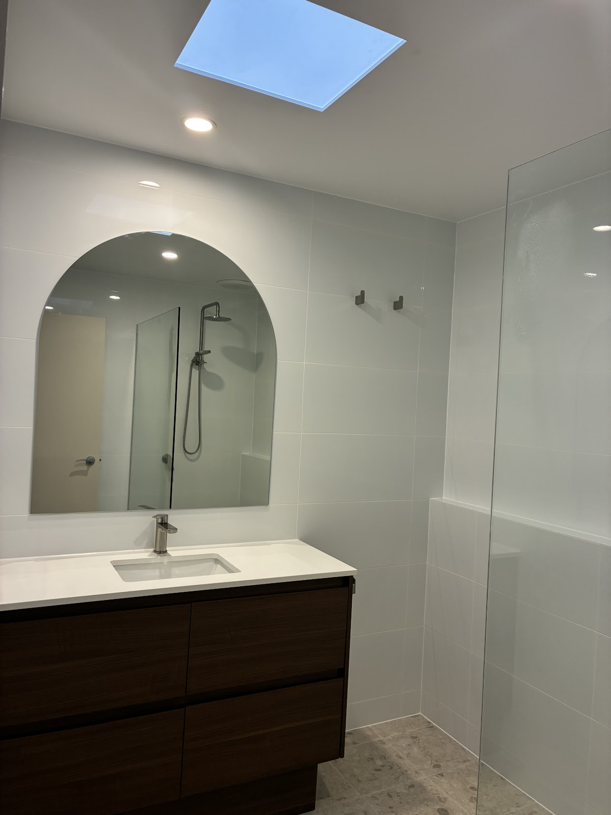Bathroom under a skylight with a dark timber vanity and arched mirror